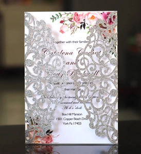 Detail of laser-cut silver glitter wedding invitation with floral insert on dark surface