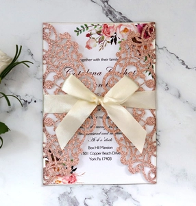 Detail of rose gold laser cut wedding invitation with ribbon on marble background