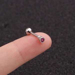 Surgical steel piercing stud with red round zircon held on a fingertip for size