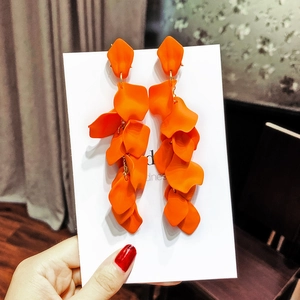 Close-up of matte orange petal drop earrings with gold hooks on a display card