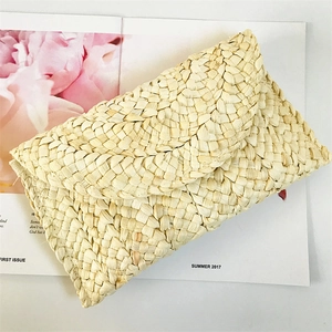 Flat lay of woven corn husk clutch bag with envelope flap on stylish magazine background
