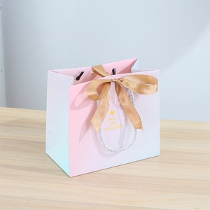 Pink and blue gradient gift bag with white rope handles and a golden silk bow decoration