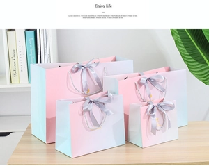 Pink and blue gradient paper gift bags in four sizes with grey ribbon bows on a desk