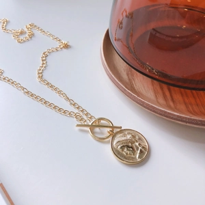 Close-up of a gold layered coin necklace with an OT toggle clasp on a white background
