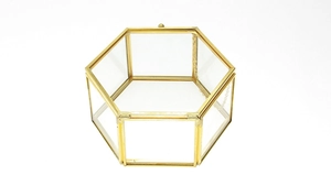 Detail view of a hexagonal glass jewelry box with a gold metal frame on a white background