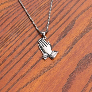 Macro shot of silver stainless steel prayer hands pendant on a box chain over wood