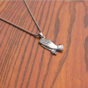 Macro shot of silver praying hands pendant with stainless steel chain on wood
