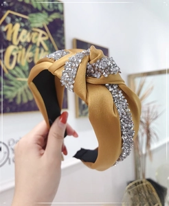 Close-up of ginger yellow knotted headband with sparkling rhinestones on satin fabric