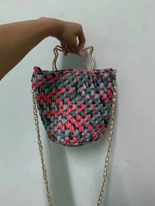 Detail of colorful woven handbag featuring cat-shaped gold handle and pearl chain strap