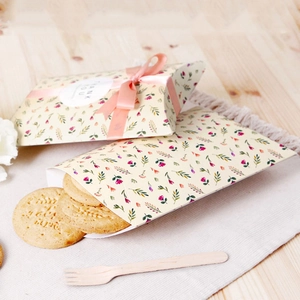 Floral paper pillow box for cookies with pink ribbon and thank you label on wood desk