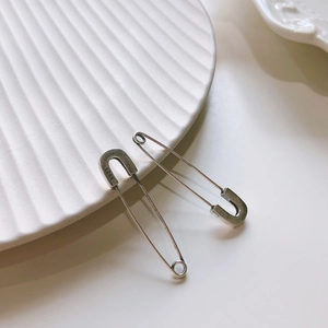 Close-up of minimalist S925 sterling silver safety pin earrings on a white ceramic plate