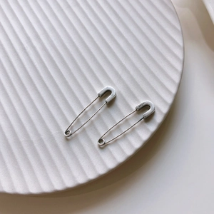 Detailed close-up of S925 sterling silver safety pin earrings on a ceramic tray
