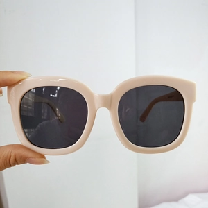 Close-up of nude pink square sunglasses with black lenses held for detail inspection