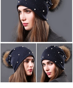Detail of dark blue knitted beanie featuring faux pearls and a large fluffy fur pompom