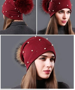 Detail of burgundy ribbed knit beanie featuring white pearls and a fluffy fur pom-pom