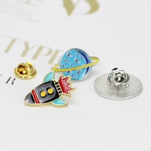 Detail of rocket and planet enamel pins with butterfly clasp on white card