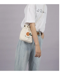 Beige canvas bucket bag with orange illustration worn crossbody over denim jeans