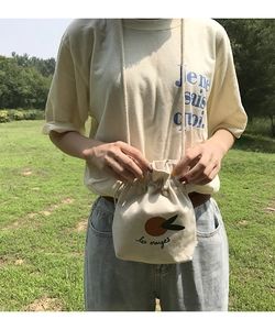 Outdoor shot of cream canvas drawstring bucket bag with orange print and French text