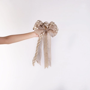 Close-up of faux linen Christmas bow with white polka dots held against a white wall
