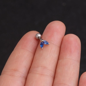Macro detail of silver marquise stud earring with blue stones on a fingertip