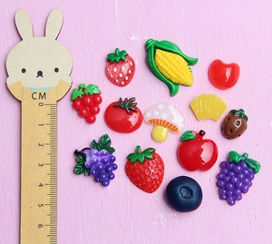 Makroaufnahme von 13 bunten Obst- und Gemüsekabochons aus Harz mit einem Hasen-Lineal