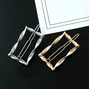Detail of twisted rectangular metal hair clips in matte gold and silver on black background
