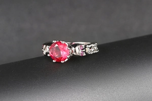 Detail of gothic silver skull ring featuring a red round center stone and purple accents