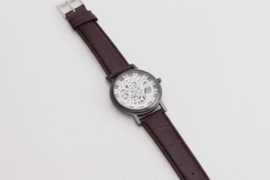 Macro detail of men's hollow dial quartz watch with brown leather strap and roman numerals
