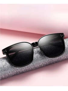 Close-up of oversized square black sunglasses with metal dot accents on a pink background