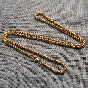 Close-up of golden stainless steel box chain necklace on grey textured linen background