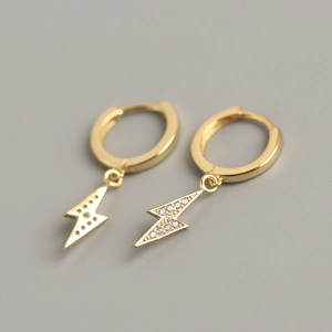 Macro detail of gold lightning bolt earrings with pavé crystals on a grey background