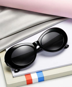 Detailed view of oval black sunglasses with glossy finish and dark UV lenses on a prop display