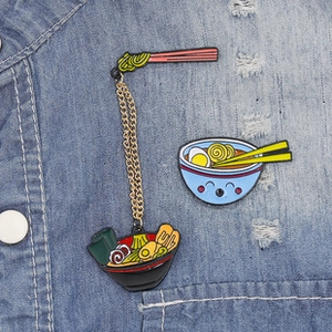 Detail of ramen enamel pins with gold chain on denim fabric showing cartoon design
