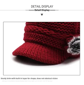 Detail view of burgundy knitted beanie with visor and soft faux fur pom-pom accent