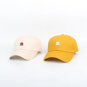 Detail of embroidered 'm' logo on beige and yellow cotton twill baseball caps