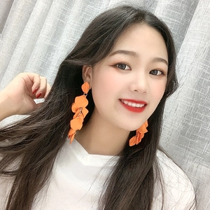 Detailed view of vibrant orange long petal earrings worn by a model in bright light
