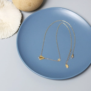 Detail view of gold paper plane necklace with star pendant on elegant blue display