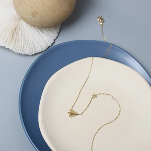 Minimalist 14K gold-plated paper airplane and star pendant necklace on ceramic plates