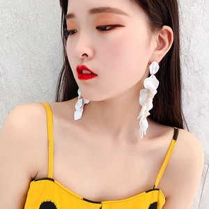Close-up of white layered rose petal drop earrings worn by a model in a polka dot dress