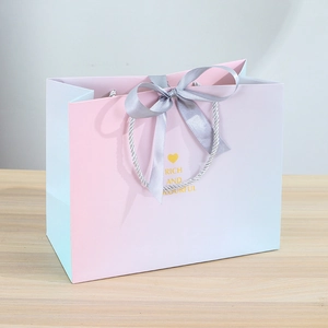 Close-up of pink and blue gradient gift bag with ribbon bow and gold lettering