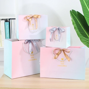 Pink and blue gradient gift bags in four sizes with ribbon handles on a desk