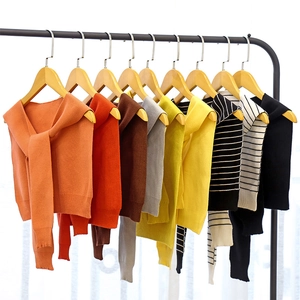Knitted shawl scarves in various colors hanging on wooden hangers against white curtains