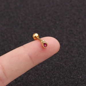 Macro shot of a golden stainless steel earring with red teardrop zircon on a fingertip