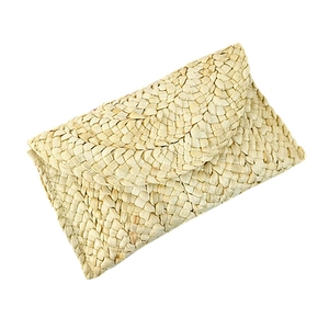 Handwoven straw clutch bag with corn husk texture and red fabric lining on white background