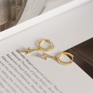 Macro shot of gold lightning bolt huggie earrings with sparkling crystals for women