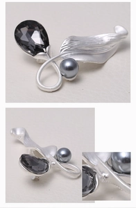 Detail of matte silver brooch with black teardrop gemstone and grey pearl accent