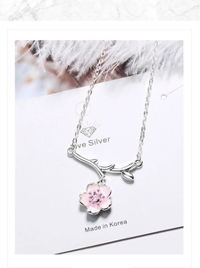 Macro shot of silver cherry blossom pendant with pink petals and purple zircon on white card
