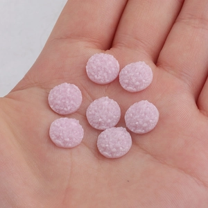 Close-up of 10mm pink resin druzy cabochons with sparkling crystal texture in hand