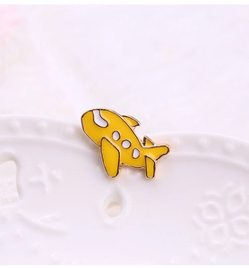 Macro shot of a yellow cartoon plane enamel pin on a white ceramic plate