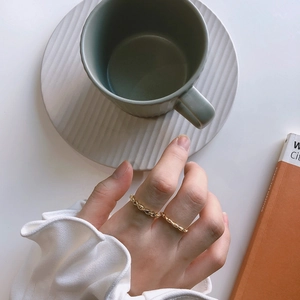 Close-up of a gold twisted rope ring worn by a model holding a grey coffee cup